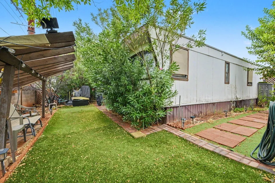 Expansive synthetic turf yard with a wood pergola structure, brick-lined pathways, and mature greenery