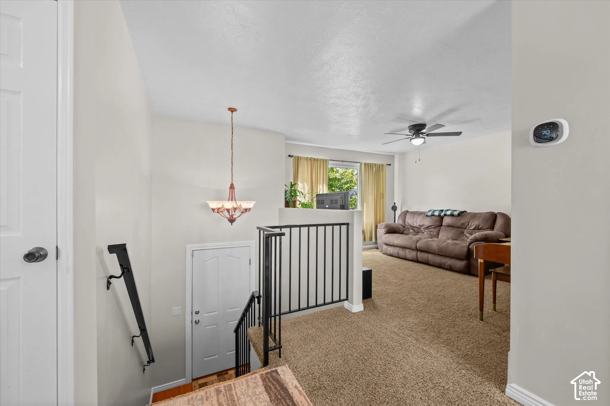 Carpeted living area featuring a ceiling fan, wall-mounted thermostat, and front door access