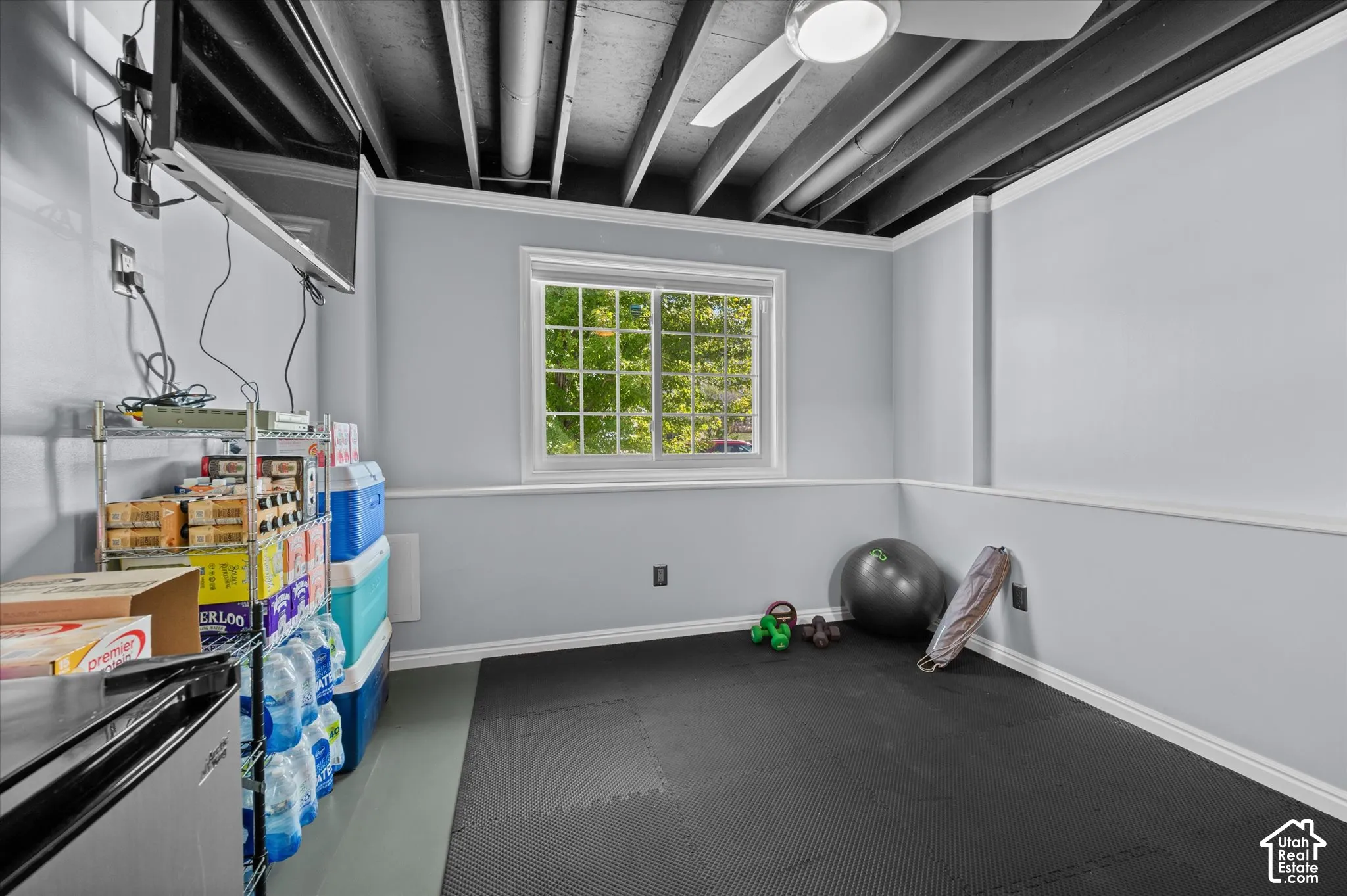 Window with white trim, light gray walls, white crown molding, exposed ceiling beams, and a ceiling fan