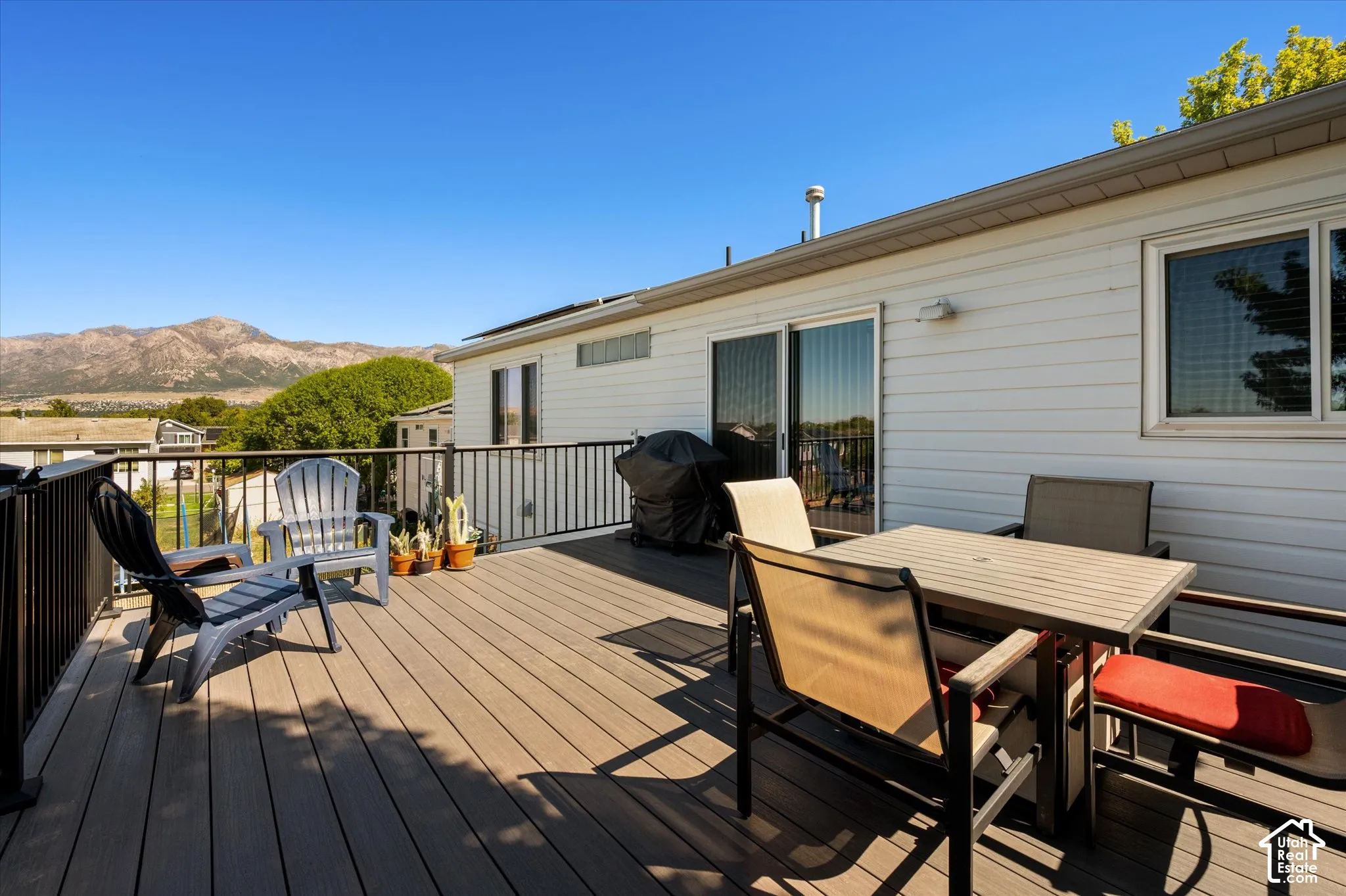 Expansive outdoor deck with mountain scenery, featuring composite decking, black metal railings, white siding, and sliding glass doors