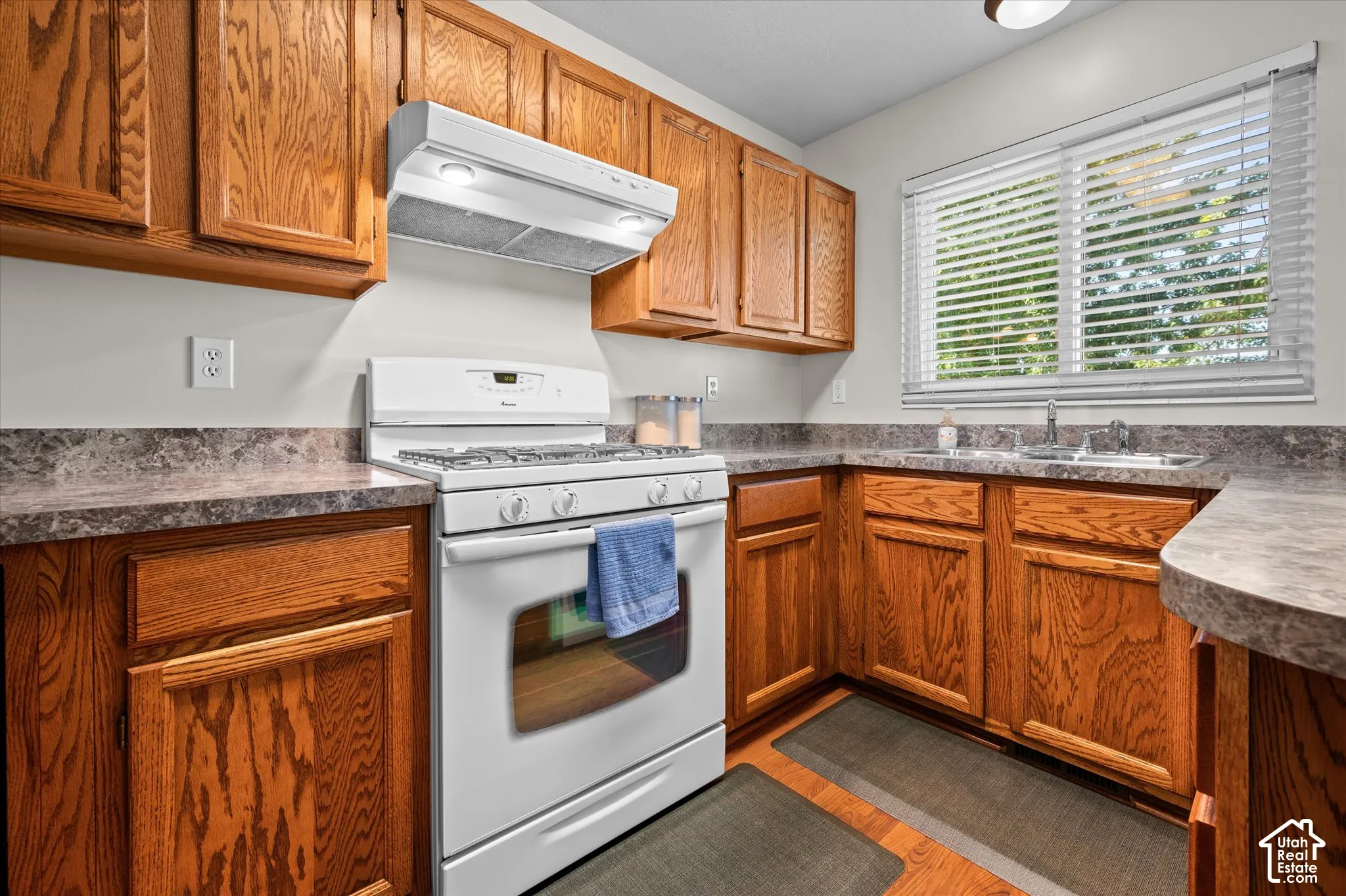 Kitchen featuring wood cabinetry, laminate countertops, a white gas range with overhead exhaust, and a double basin stainless steel sink