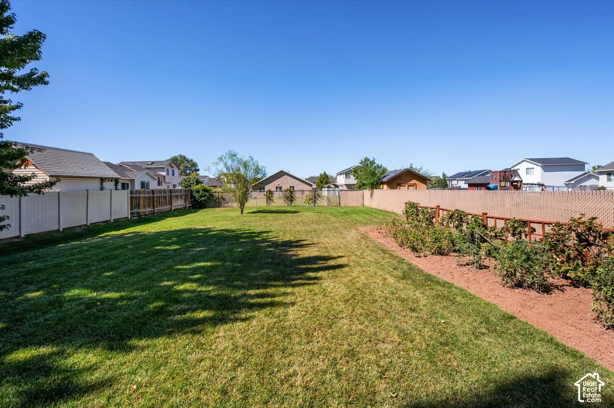 Expansive backyard featuring a lush lawn, established garden beds, and a perimeter fence