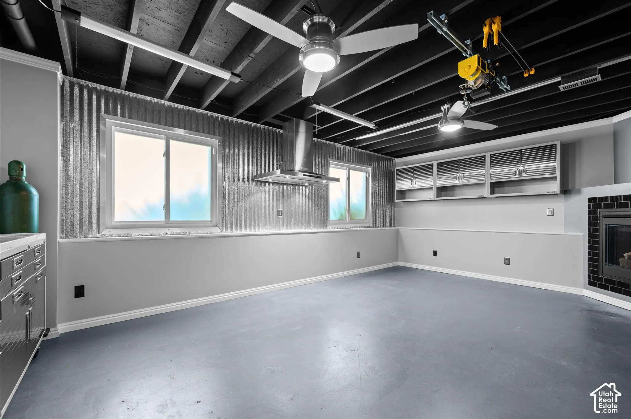 Corrugated metal accent wall, exposed ceiling beams, two ceiling fans with integrated lighting,  and a fireplace with a black tile surround