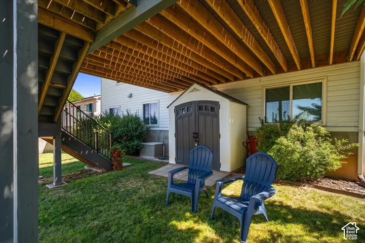 Covered patio area with a slatted wood ceiling, a built-in storage shed, and a composite staircase with metal railings