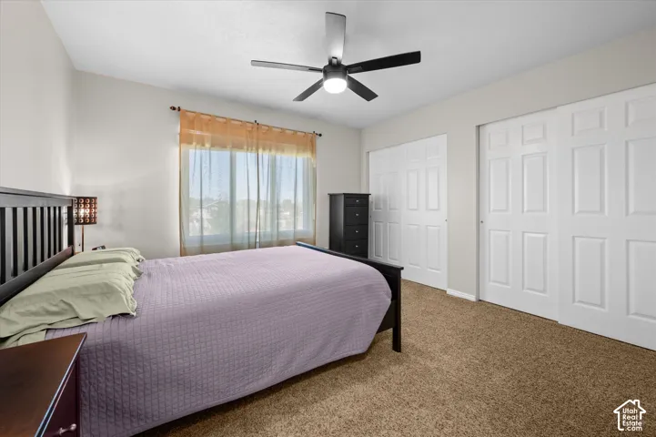 Carpeted room featuring a ceiling fan with integrated lighting, a window with sheer curtains, and two sets of bi-fold closet doors