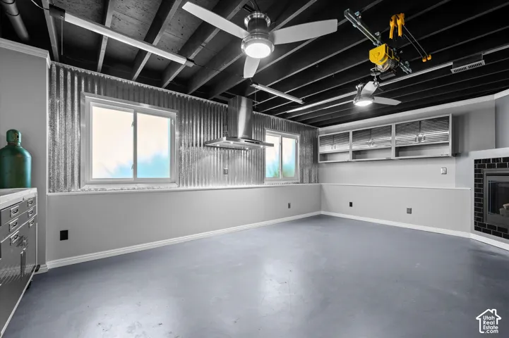 Corrugated metal accent wall, exposed ceiling beams, two ceiling fans with integrated lighting,  and a fireplace with a black tile surround