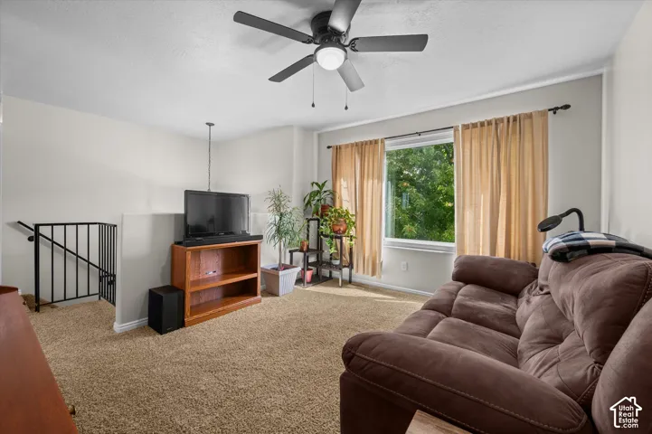 Ceiling fan with integrated lighting, carpeted flooring, white trim, rectangular window, and black metal railing