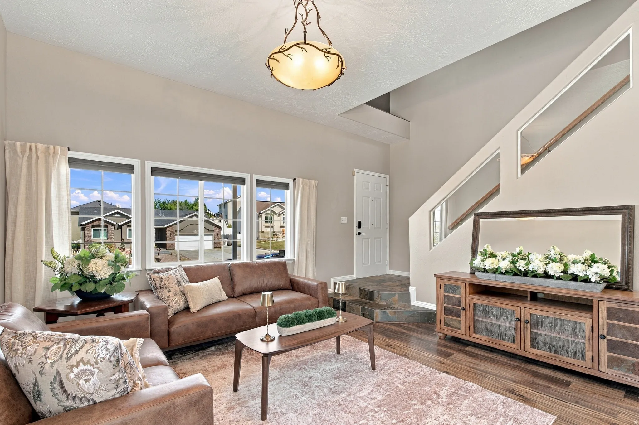 Living room with extra high ceilings, big windows with custom cellular shades, beautiful wood laminate and stone flooring.