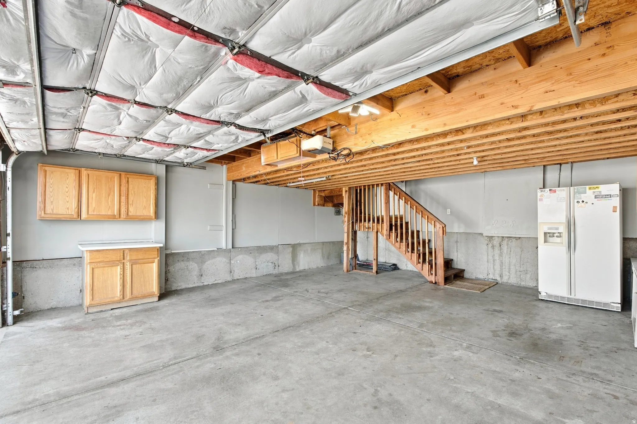 Two car attached garage with cabinets, second refrigerator and stairs going up to custom loft and into the kitchen.