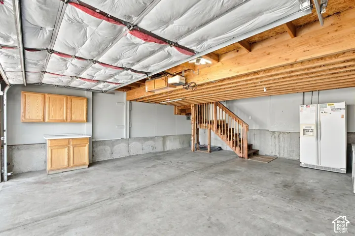 Two car attached garage with cabinets, second refrigerator and stairs going up to custom loft and into the kitchen.