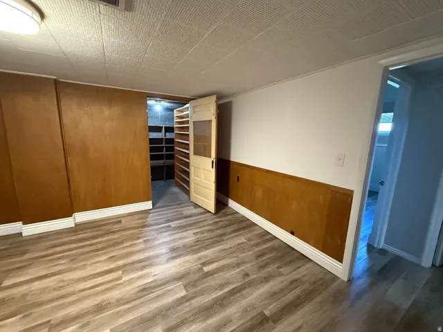 Wood-finish flooring, wood paneling, white walls, built-in shelving, and a paneled door with glass insert