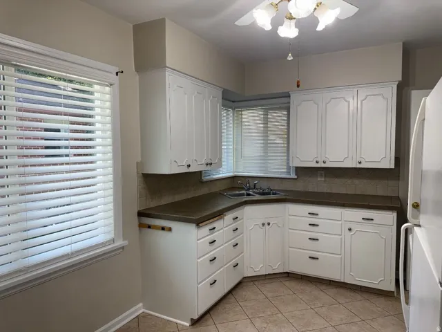 White cabinetry with black hardware, corner double basin sink, tile backsplash, and light-toned tile flooring