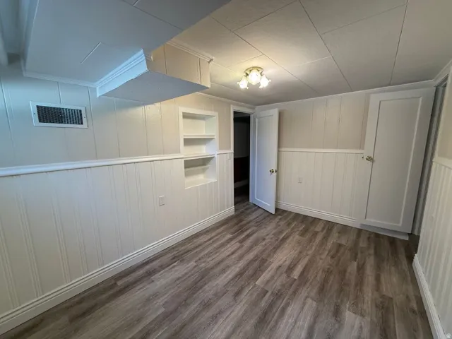 Wood-finish flooring, white paneled wainscoting, recessed shelving, ceiling-mounted lighting, and a white paneled door