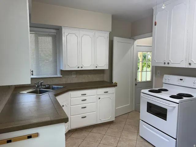 Kitchen featuring white cabinetry, a double basin stainless steel sink, brown countertops, and tile flooring