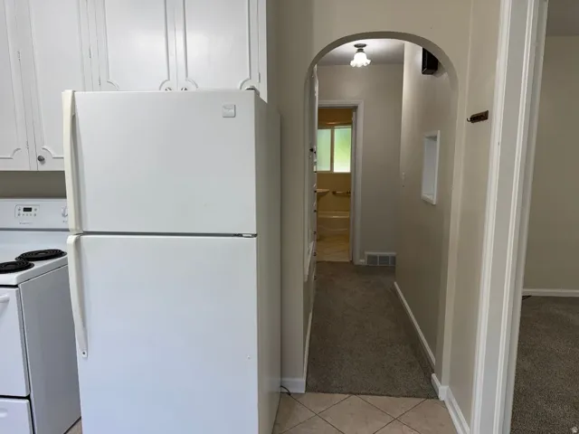 White refrigerator and range, upper cabinetry, arched hallway entry, and tiled flooring