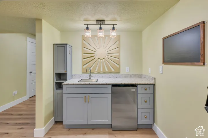 Built-in kitchenette featuring a stainless steel sink, light grey cabinetry with gold-tone hardware, a stainless steel undercounter appliance, and a speckled countertop