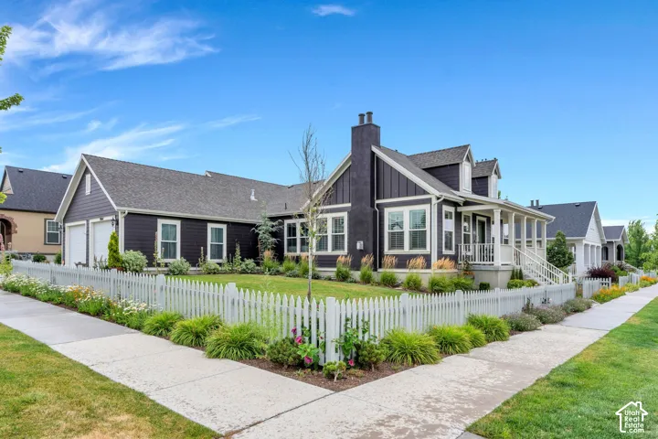 Dark-toned exterior featuring white trim, a covered porch, an attached two-car garage, and a white picket fence