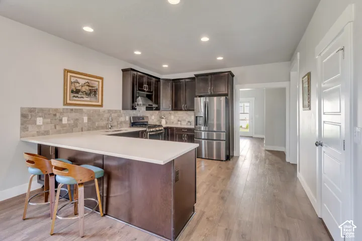 Kitchen featuring dark wood cabinetry, stainless steel appliances, a tile backsplash, and a breakfast bar with a light-colored countertop