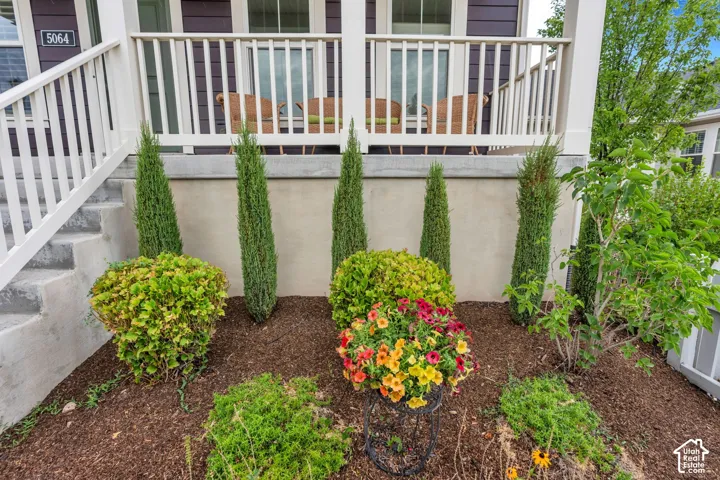 Front porch with white railings, concrete steps, and a decorative garden bed