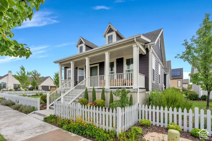 Siding exterior with dormer windows, covered front porch, white picket fence, and established landscaping