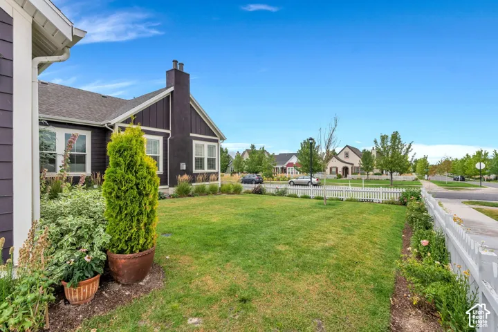 Manicured lawn with a white picket fence, bordered by mature landscaping and a paved sidewalk