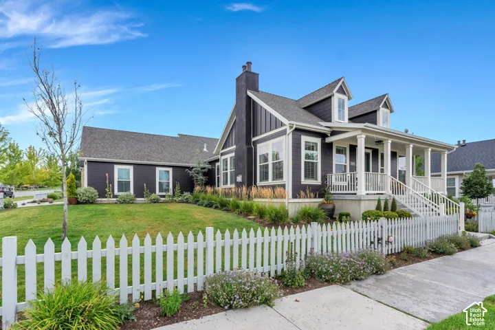 Dark-toned siding exterior with white trim, a covered porch with white columns and railing, a white picket fence, and a manicured lawn