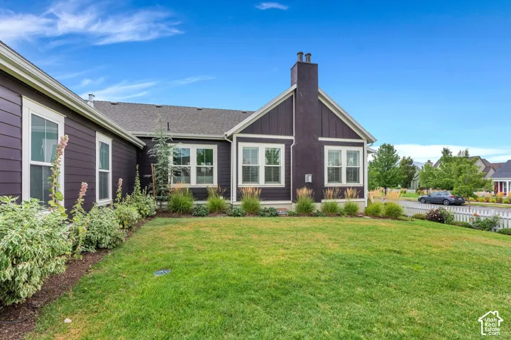 Dark-toned siding with white trim, multiple windows, a prominent chimney, a gabled roof, and a green lawn