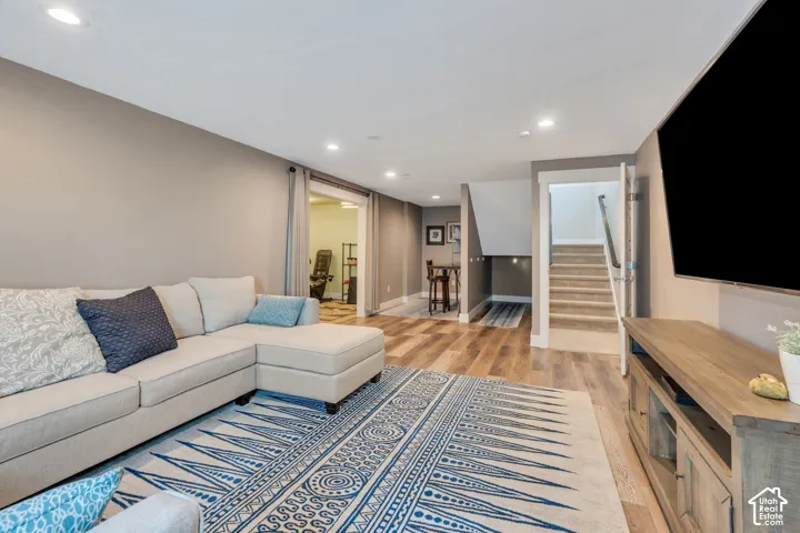 Recessed ceiling lighting, wood-finish flooring, sliding barn door, staircase with carpeted treads, and built-in media console