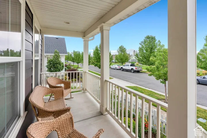 Covered front porch with concrete flooring, white column supports, and slatted railings