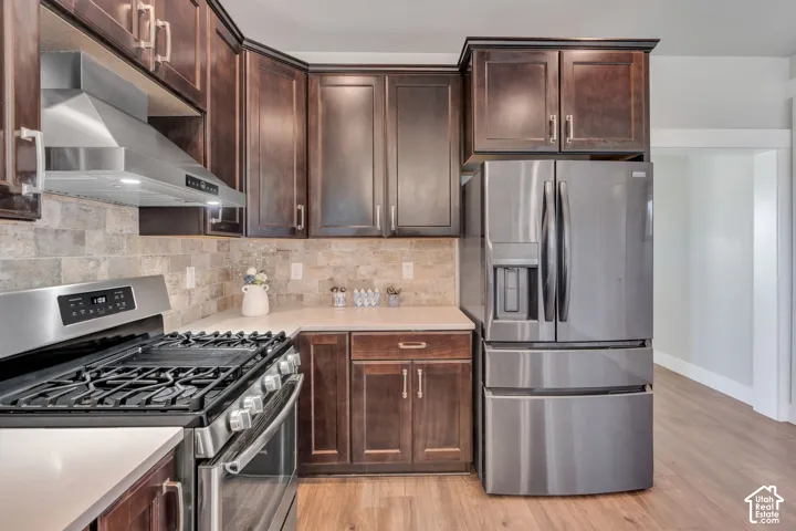 Contemporary kitchen featuring dark wood cabinetry, stainless steel appliances, light-toned countertops, a tile backsplash, and wood-finish flooring