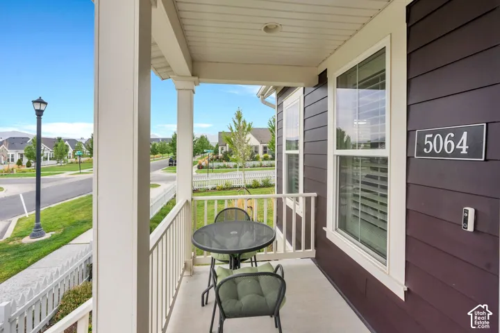 Covered porch with white railings and columns, featuring a deep plum-toned siding facade, white-framed windows with louvered blinds, and a visible address plaque