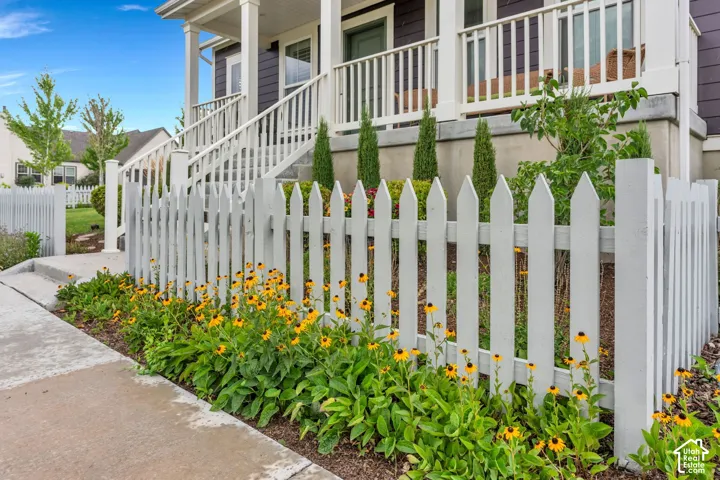 Front porch with white railings, white picket fence, concrete walkway, and landscaping with flowering plants