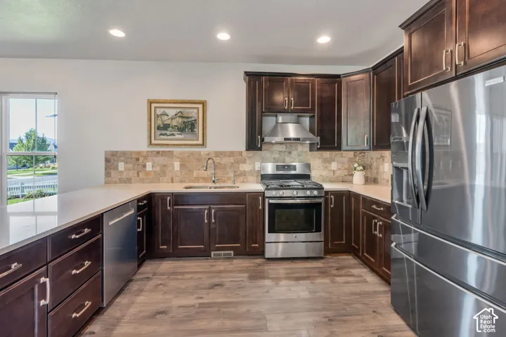 Contemporary kitchen featuring stainless steel appliances, dark wood cabinetry, light countertops, and wood-finish flooring
