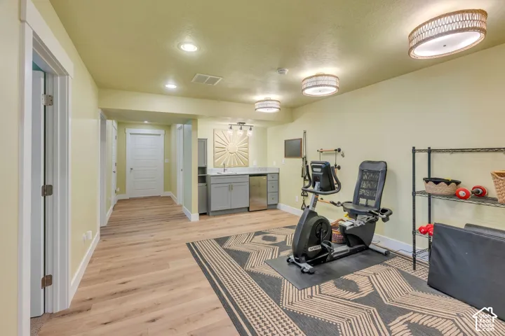 Wood-finish flooring, recessed lighting, and a built-in wet bar with a stainless steel sink and refrigerator