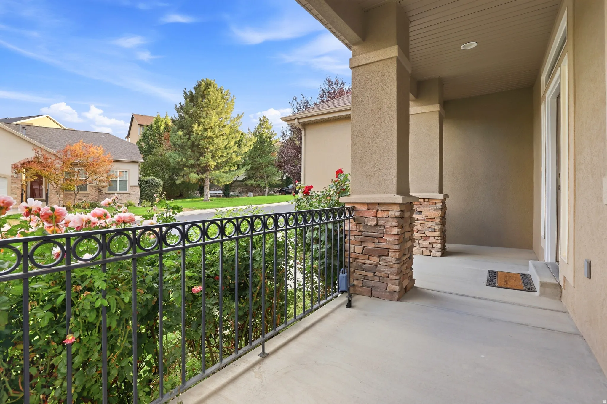 Front porch with stone-clad columns, stucco exterior, and concrete flooring