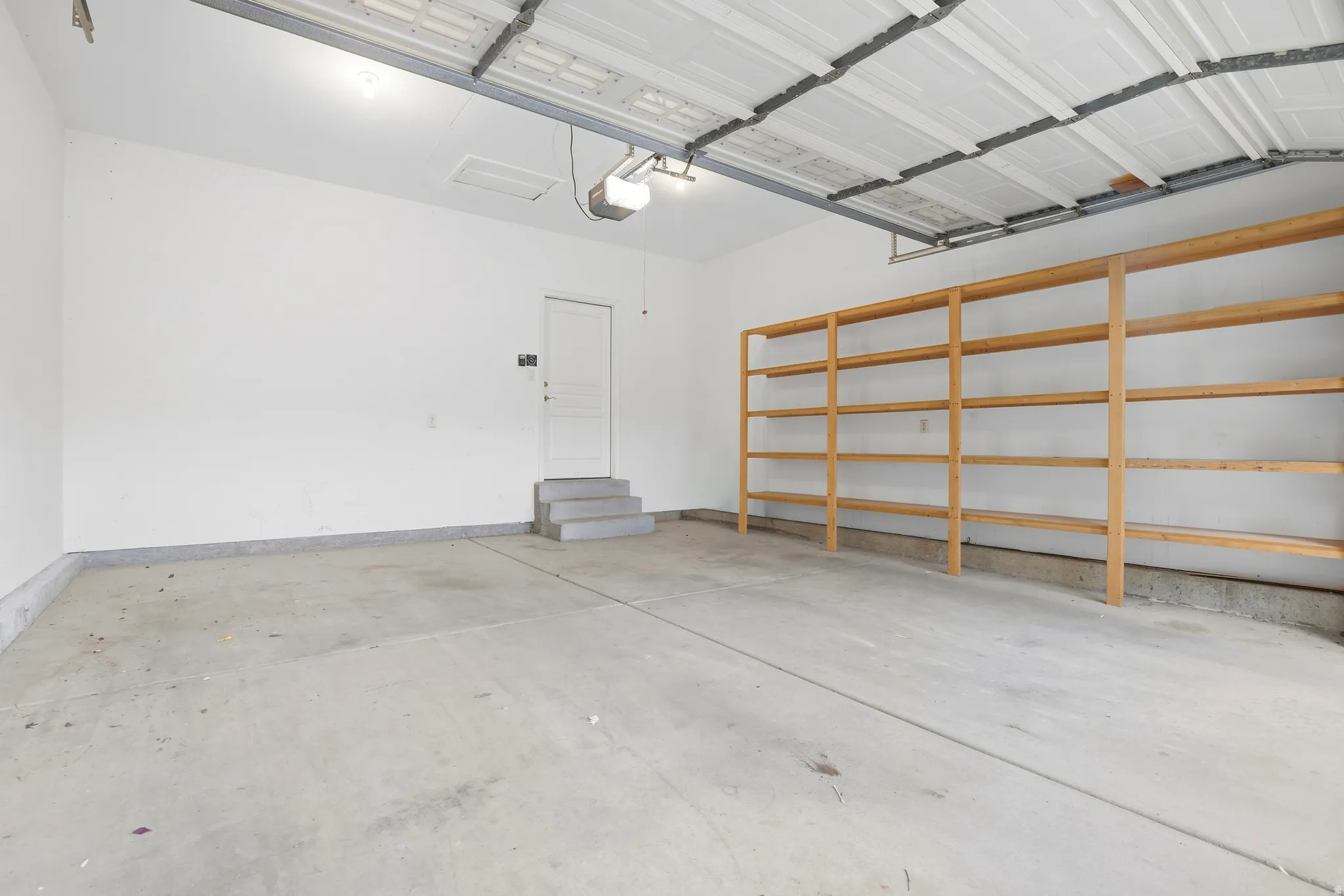 Garage featuring concrete flooring, built-in wooden shelving, and a pedestrian door with steps