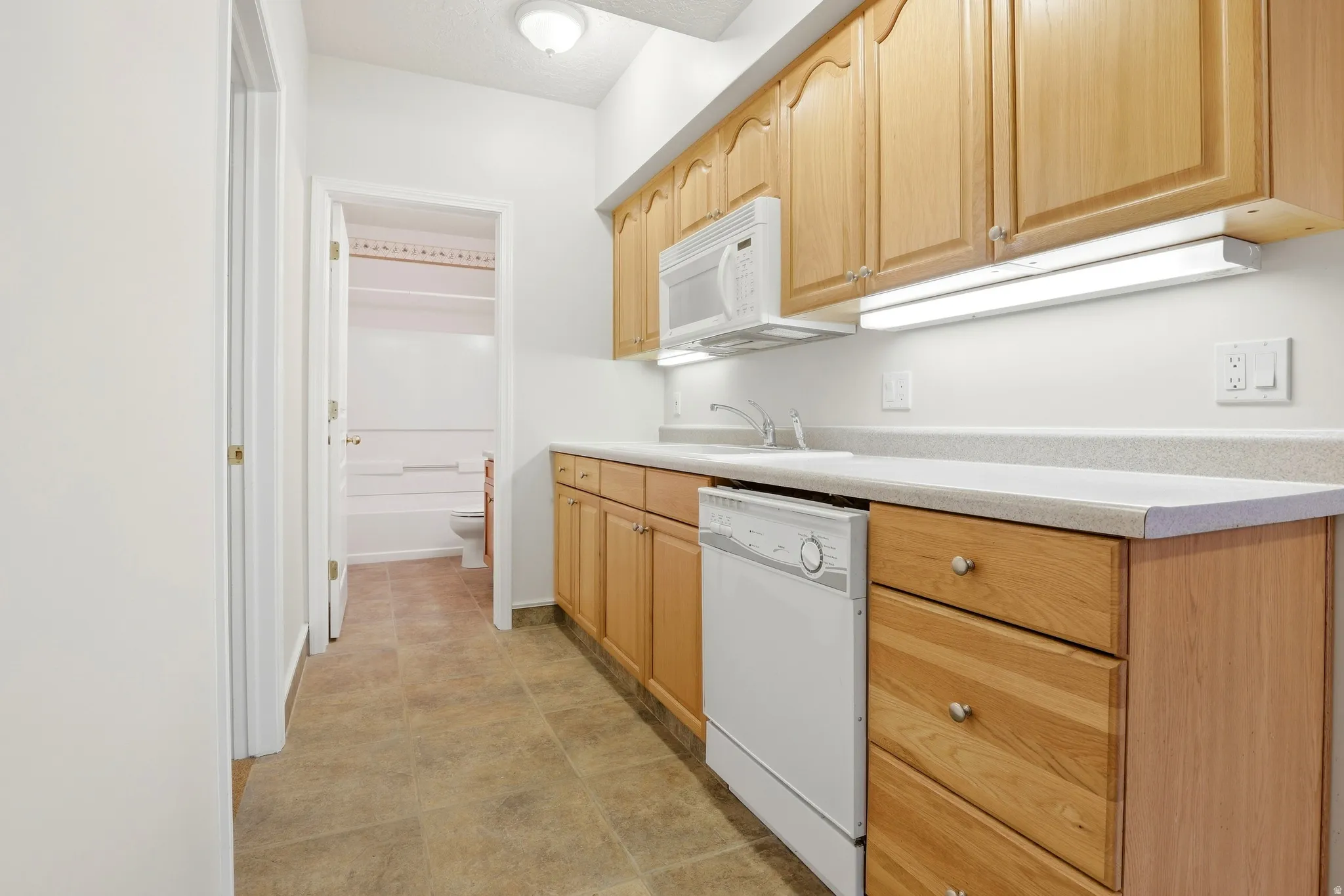 Galley kitchen with wood-finish cabinetry, light-toned countertops, and tile flooring
