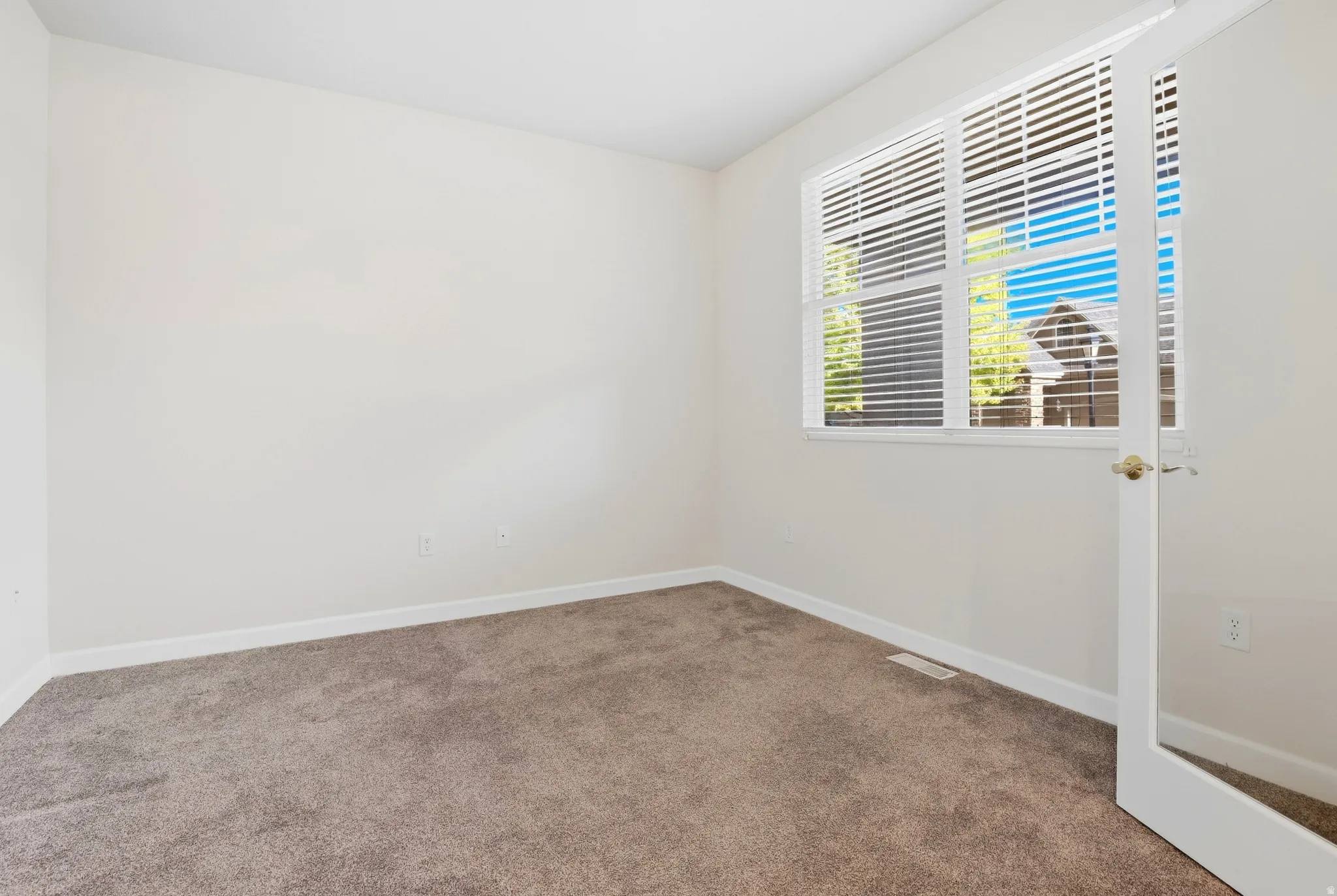 Neutral-toned carpeting, ample natural light, white trim, and a window with horizontal blinds
