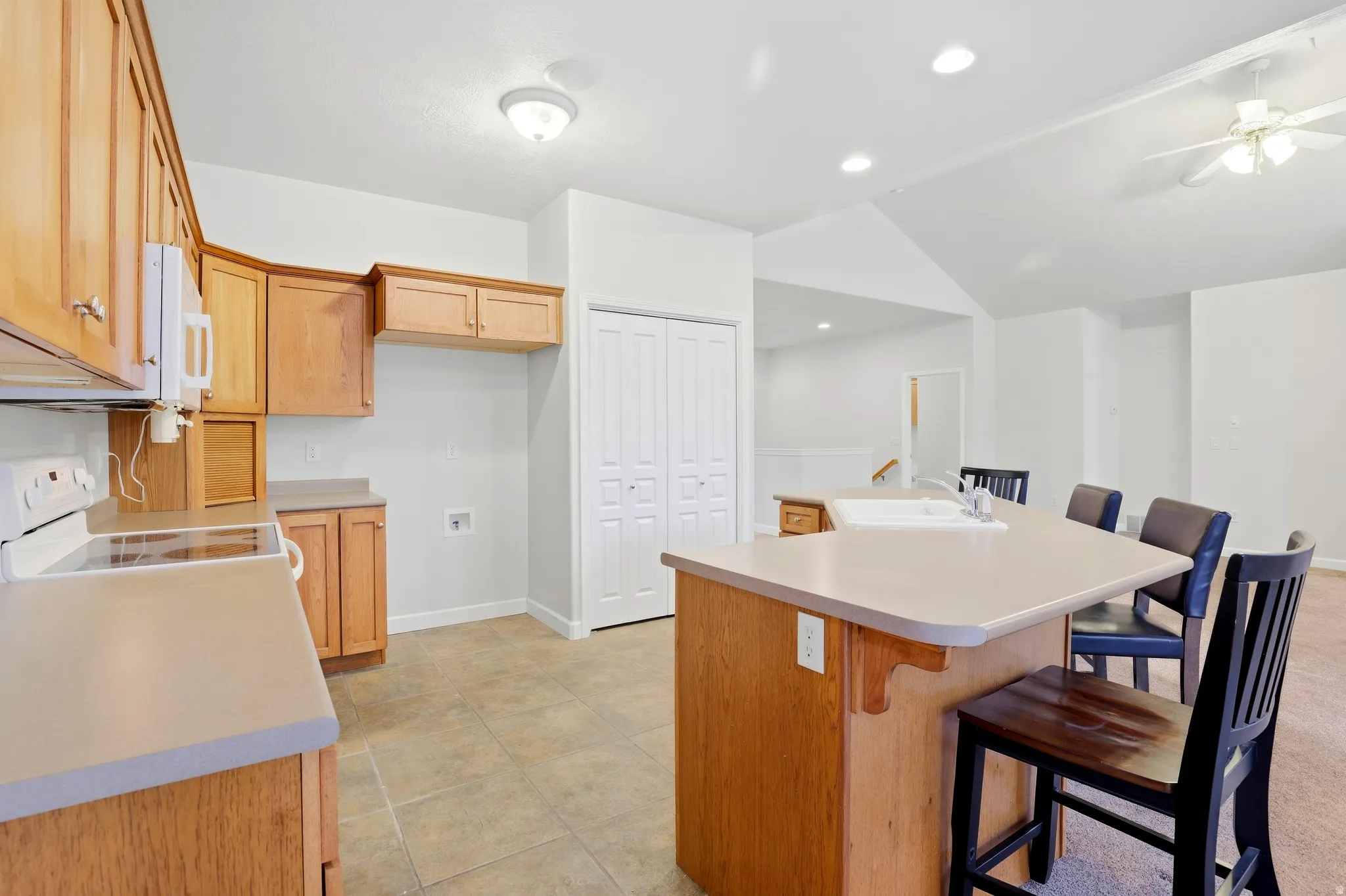 Kitchen featuring light wood cabinetry, white appliances, and a central island with an integrated sink and breakfast bar