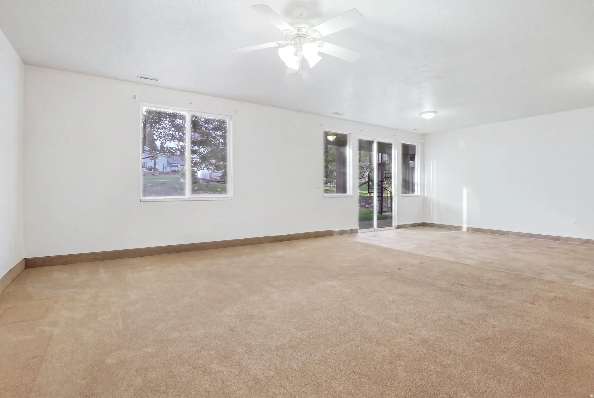 Spacious room featuring carpeted and tiled flooring, a ceiling fan, and sliding glass doors