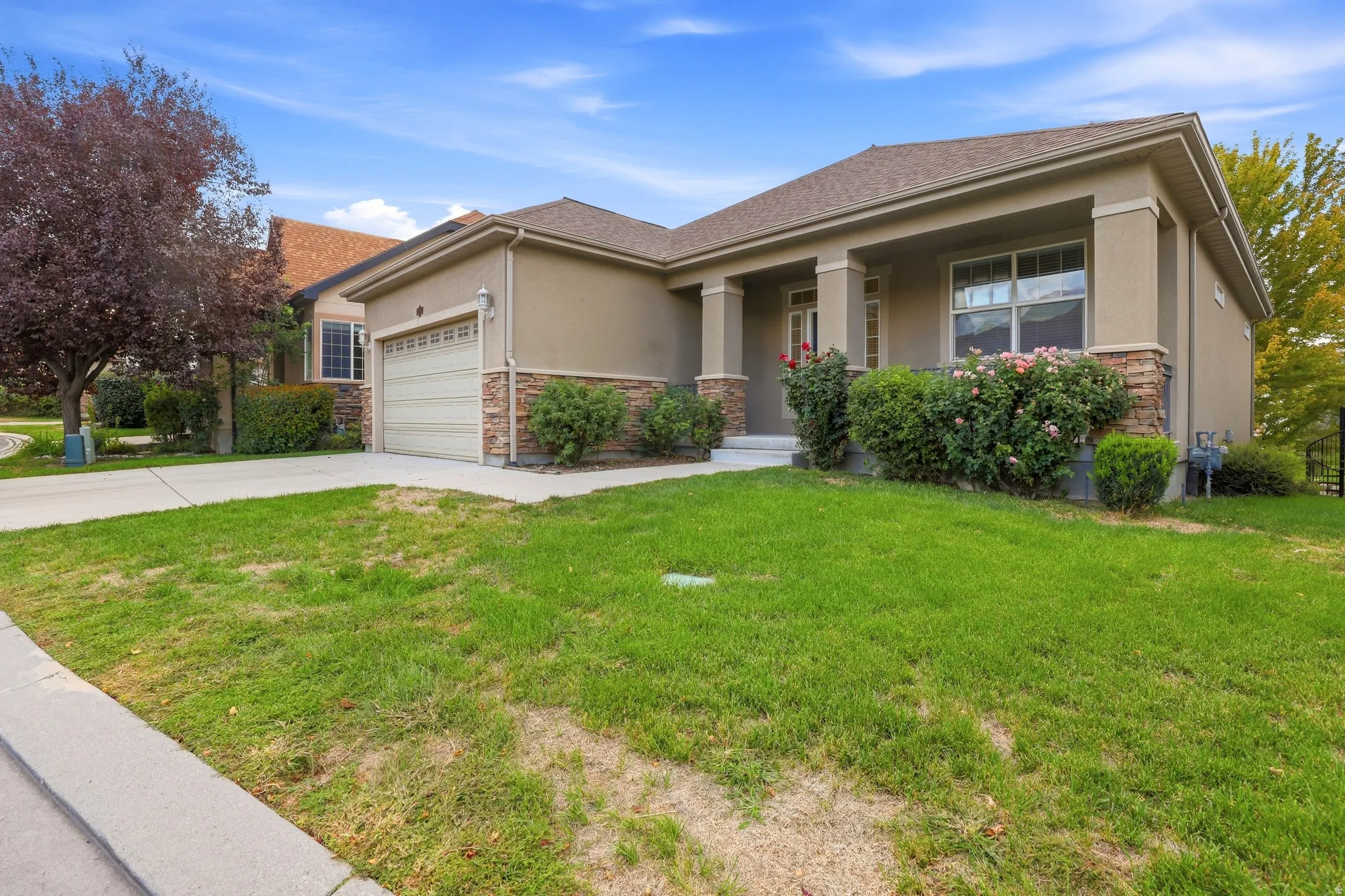 Stucco exterior with stone accents, covered entry, attached garage, and mature landscaping