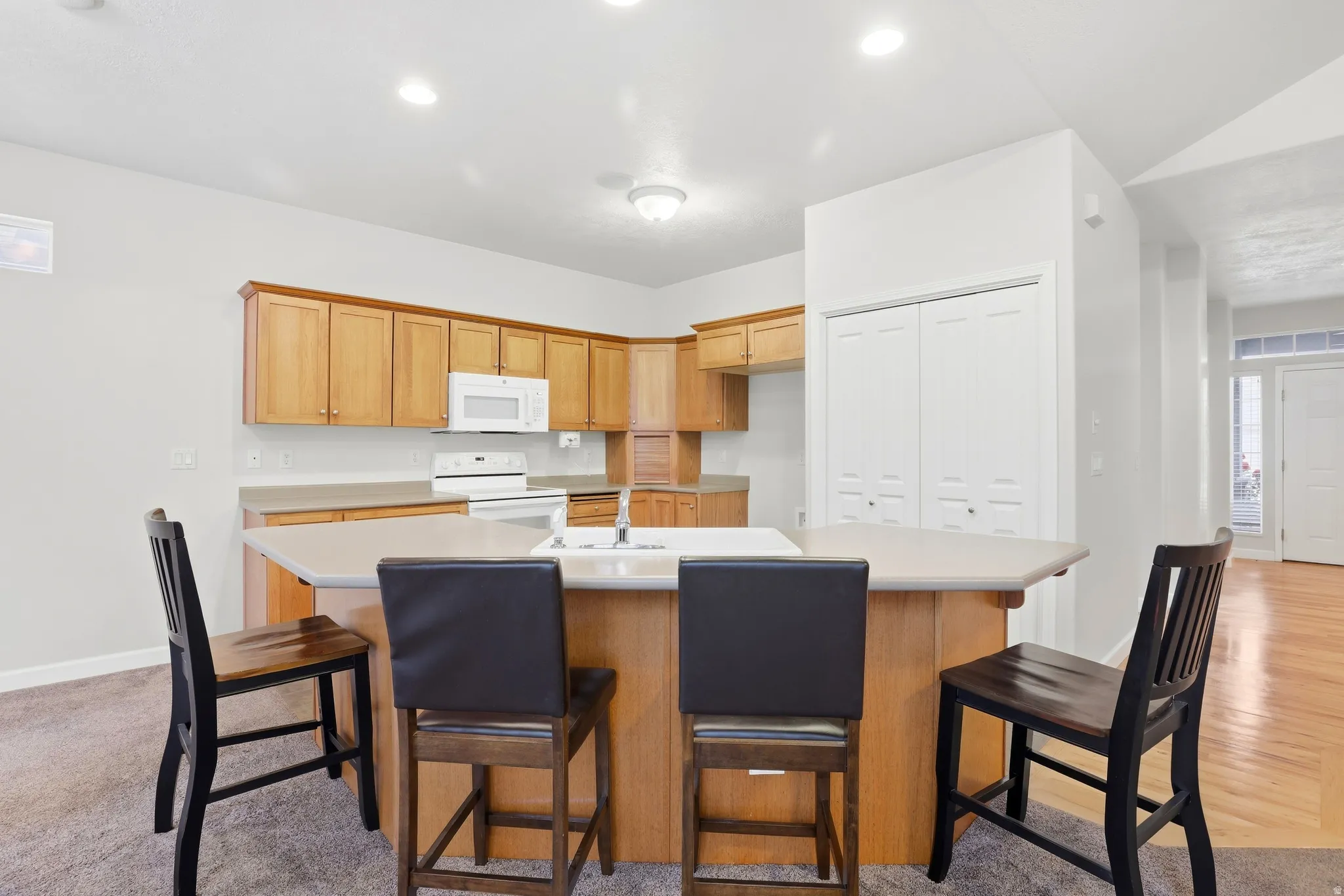 Kitchen featuring wood cabinetry, white appliances, a center island with sink, and overhead recessed lighting