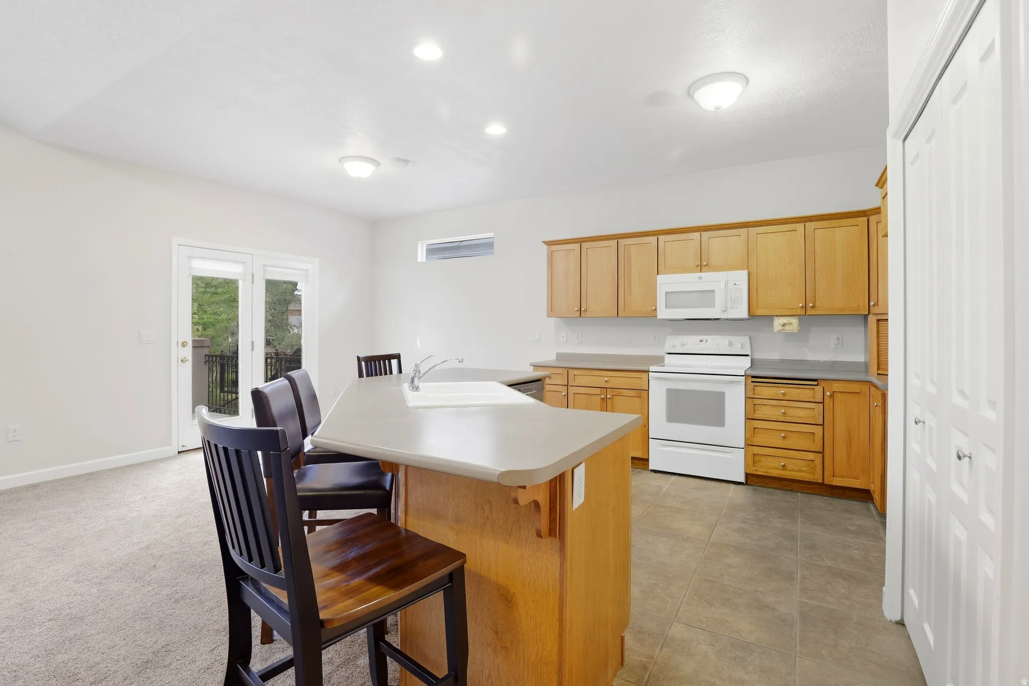 Kitchen featuring wood cabinetry, white appliances, a center island with a sink, and tile flooring
