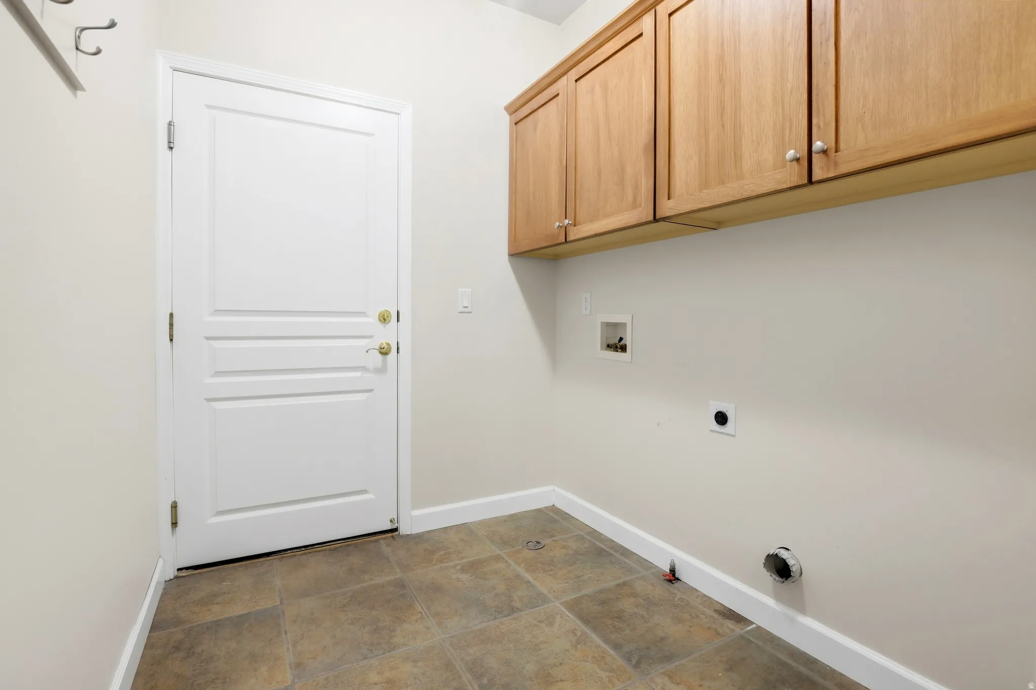 Tile flooring, white paneled door, overhead natural wood cabinetry, and laundry hookups