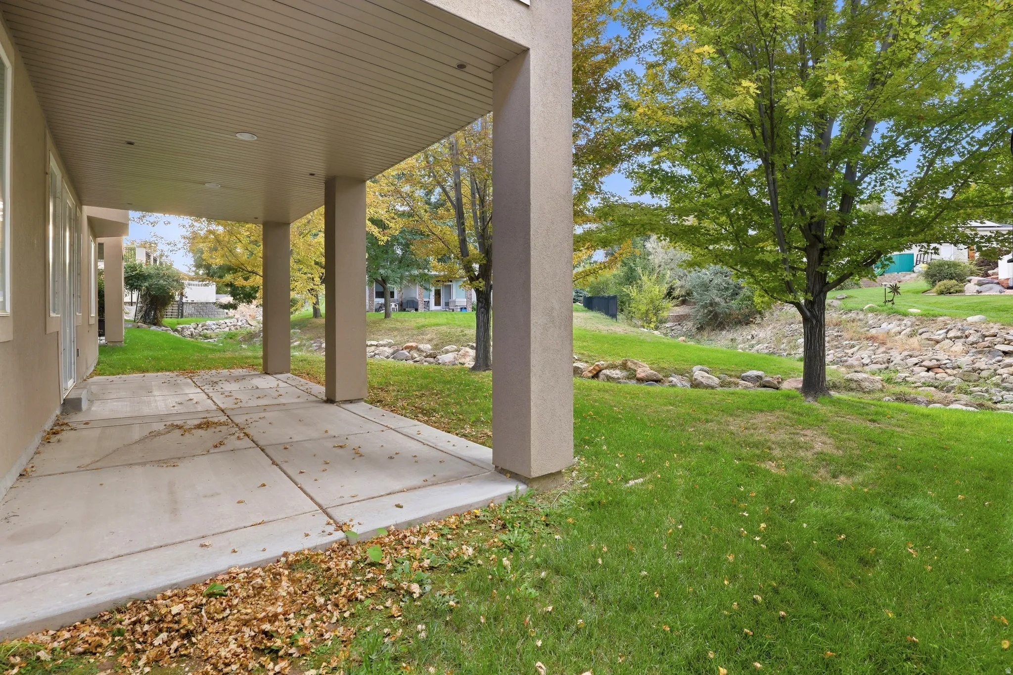 Covered patio with recessed lighting, concrete flooring, and direct access to a landscaped yard with mature trees and a rock-lined feature