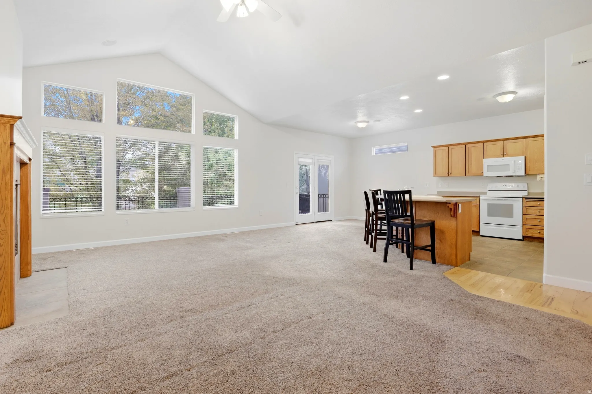 Vaulted ceiling with a ceiling fan, wall of windows, double French doors, wood-finish flooring, and a kitchen featuring wood cabinetry