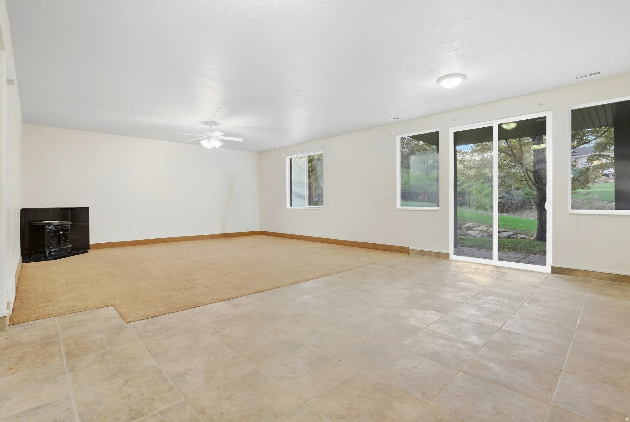 Expansive room featuring mixed flooring with carpeting and tile, a built-in fireplace unit, and a ceiling fan