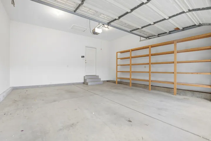 Garage featuring concrete flooring, built-in wooden shelving, and a pedestrian door with steps