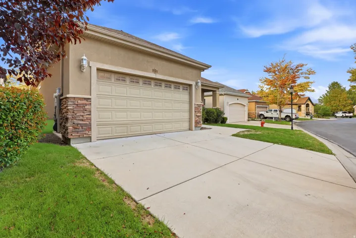 Stucco exterior with stone accenting, two-car garage, concrete driveway, and established front landscaping