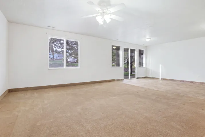 Spacious room featuring carpeted and tiled flooring, a ceiling fan, and sliding glass doors